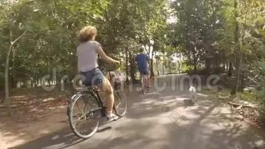 在公园里骑自行车的一对年轻快乐的嬉皮士夫妇和<strong>宠物</strong>狗在附近奔跑。 <strong>高清</strong>，慢动作。